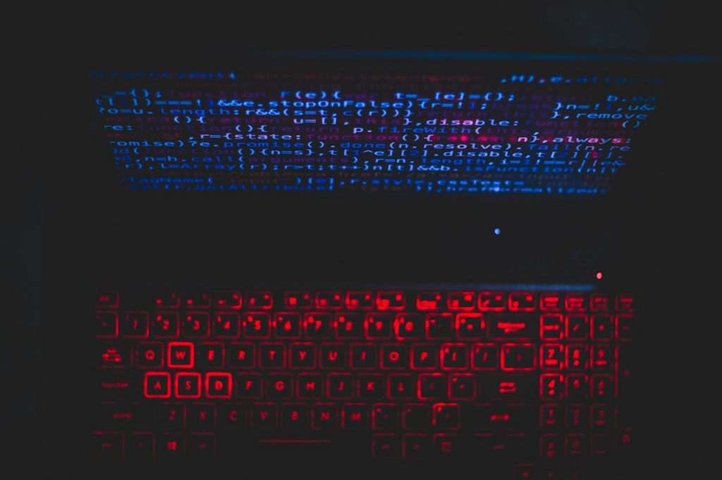 Dark-themed laptop setup with a red glowing keyboard and code on screen, ideal for tech enthusiasts.
