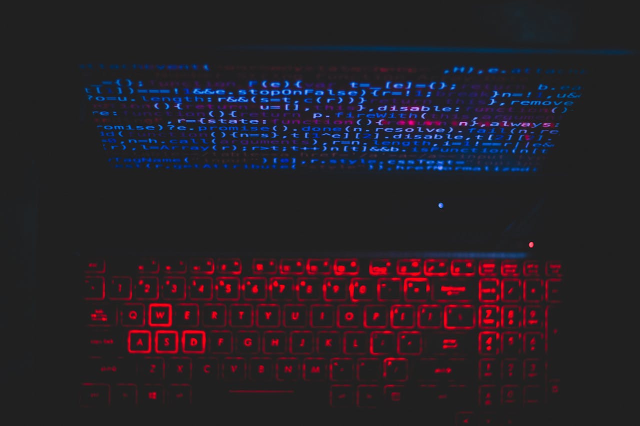 Dark-themed laptop setup with a red glowing keyboard and code on screen, ideal for tech enthusiasts.